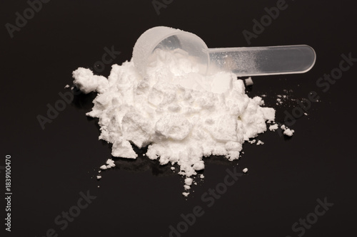 A scoop of creatine monohydrate powder on a black reflecting surface. Used by fitness enthusiast and recreational bodybuilding. 