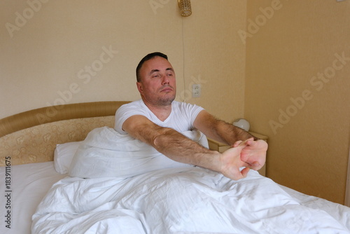Man waking bed man wearing sleepwear waking up in bed and stretching his arms in bedroom at home. male person doing morning exercises for health indoors. High quality 4k footage
