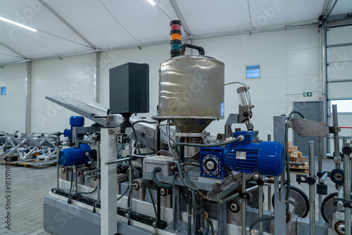 Industrial extrusion or processing machine with stainless hopper and blue electric motor in factory hall