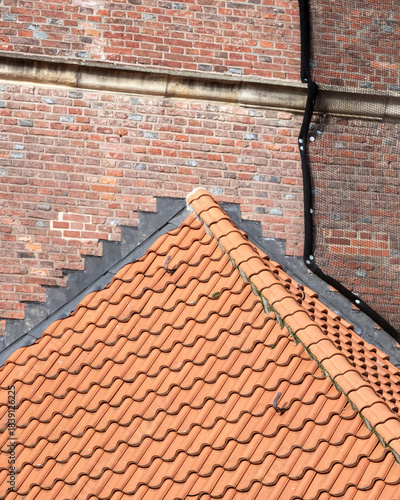 View of a terracotta roof with textured tiles against a brick wall in a historic neighborhood during daylight