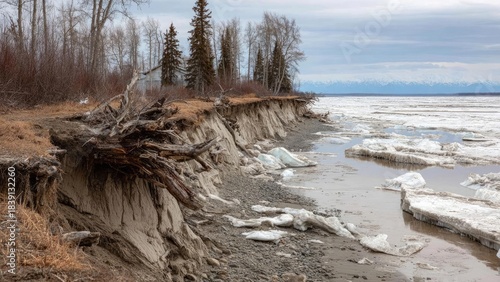 Shoreline eroded, exposing tree roots; a small house sits among bare trees as ice floes drift on a cold lake. Concept Shoreline erosion, Exposed tree roots, Isolated lakeside cottage