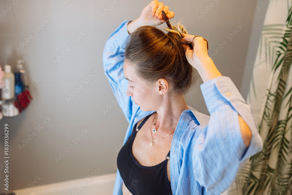 Naklejka premium Woman meticulously ties her hair in bathroom mirror reflection