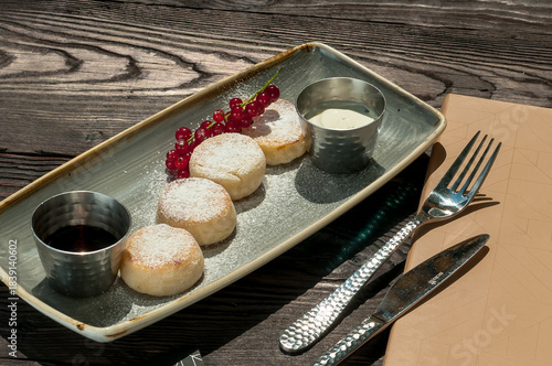 breakfast cheesecakes on a plate with sour cream and sauce and a sprig of currants on the table