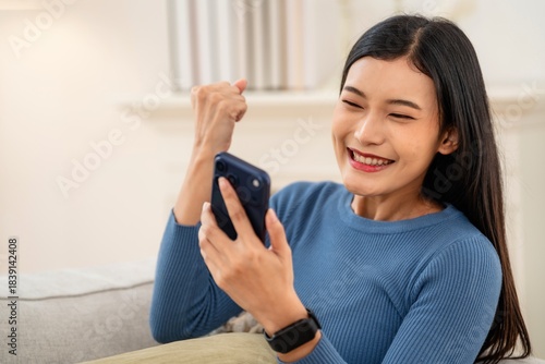 Joyful moment of a woman celebrating success while using her phone at home during the afternoon