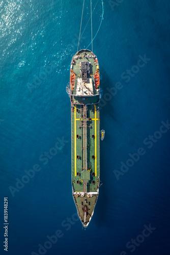 Aerial view of a ship sailing through the deep blue sea, the vessel's green and yellow deck contrasting with the surrounding water, Salina, Sicilia, Italy.