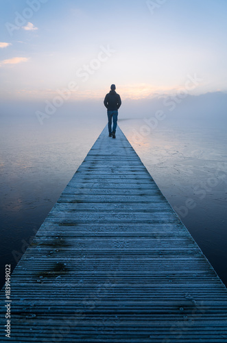 A man walking alone on a jetty during a foggy, autumn dawn.