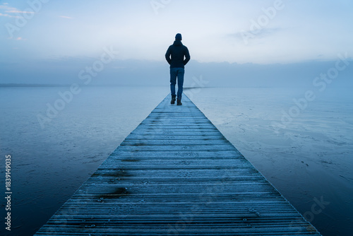 A man walking alone on a jetty during a foggy, autumn dawn.
