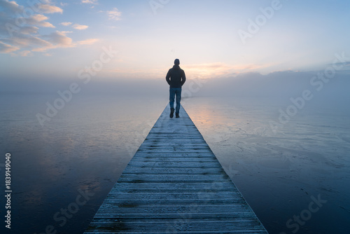 A man walking alone on a jetty during a foggy, autumn dawn.