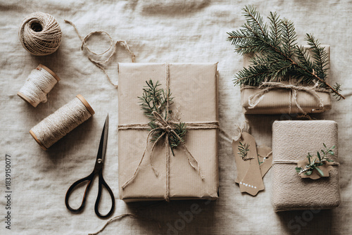Neutral Eco-Friendly Holiday Gift Wrapping Flat Lay with Kraft Paper, Twine and Evergreen on Light Textured Background