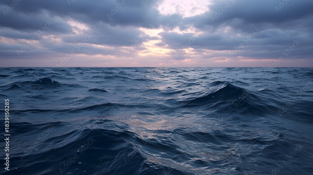 Obraz premium Dramatic seascape with turbulent ocean waves under a moody overcast sunset sky with hints of glowing light