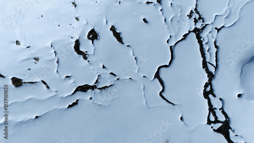 Aerial view of a stark, snow-covered landscape, where the crisp white expanse is dramatically fractured by dark, winding crevices, Wildhaus-Alt Saint Johann, St. Gallen, Switzerland.