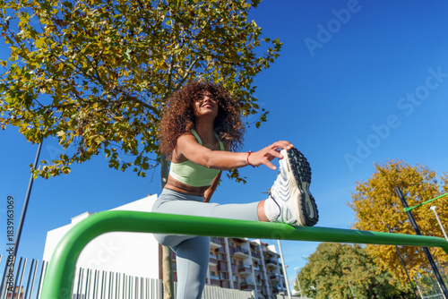 Young woman performing a warm up stretch on a horizontal bar, preparing for a workout against a clear blue sky