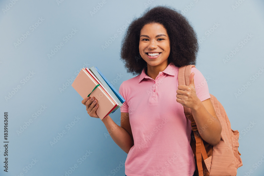 Obraz premium Young African American student smiling holding books and giving thumbs up