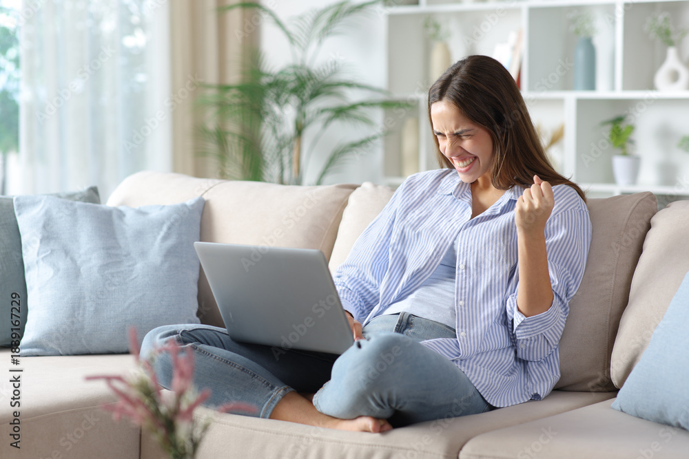 Fototapeta premium Excited woman in blue celebrating good news checking laptop
