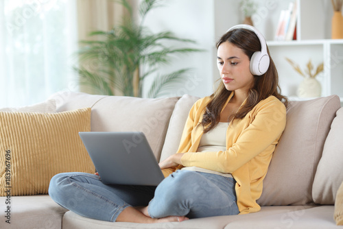 Serious woman in yellow watching media on laptop