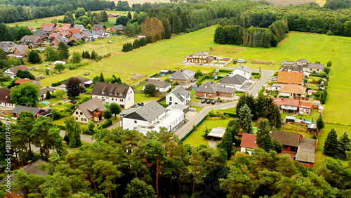 Aerial view of a peaceful residential area with houses, green fields, and forests, showing suburban development and living