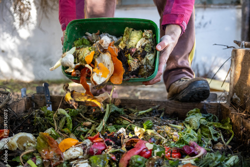 Person's hands tipping a container of kitchen waste into a garden compost heap
