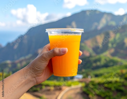 Bright orange juice held against a lush, green mountain backdrop with blue skies