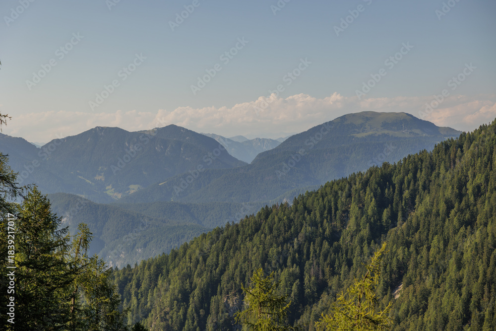 Fototapeta premium vista dettagliata di varie catene montuose ricche di verdi foreste, che si estendono verso l'orizzonte, tra l'Italia e l'Austria, di giorno, con meteo sereno, in estate