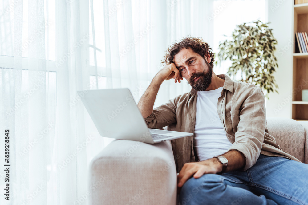 Fototapeta premium Thoughtful Man Working From Home On Laptop In Cozy Living Room Setting