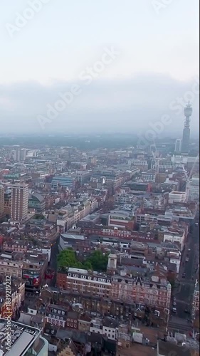 4K aerial vertical video of London skyline featuring the BT Tower in fog. Cinematic drone footage of Fitzrovia rooftops and gloomy city atmosphere. Ideal for travel reels and moody mobile content.