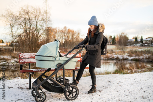 Stroller with brake on. Mother and baby in winter. Pram security. Buggy and carriage safety. Busy mom outdoor in park with snow in Finland.