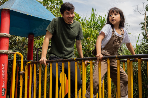 Side view of a man and his niece hanging and playing cheerfully on the bars of a playground, a dynamic and fun outdoor scene