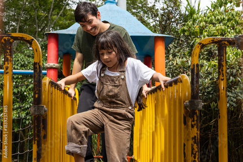 Front view of a man with his niece playing, hanging from the bars in a playground, a cheerful and fun outdoor scene showing playfulness, energy, and family bonding