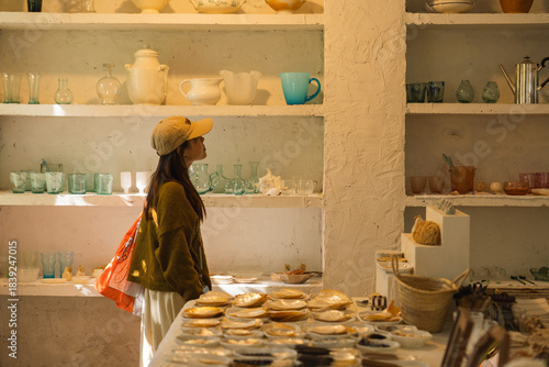 Young woman in cap browsing ceramic and glass goods displayed on shelves and tables indoors