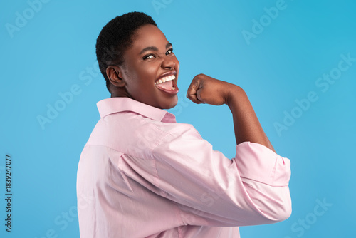 Foto A person with a short black hairstyle smiles joyfully while flexing their arm in a gesture of strength