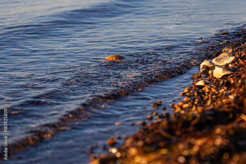 Close-up of a rocky shoreline with gentle waves lapping against the stones at sunset.
