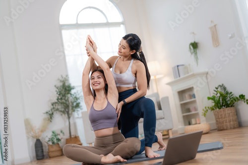 Two women practice yoga together in a bright indoor space with a laptop on the floor in the afternoon