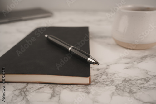 Wallpaper Mural A black notebook and pen rest on a smooth marble table beside a white coffee cup filled with dark coffee. This scene captures a peaceful moment for creativity Torontodigital.ca