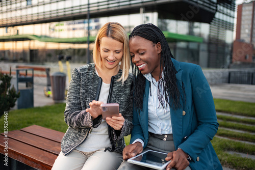Fotografija Businesswomen smiling, sharing smartphone content outdoors in urban setting