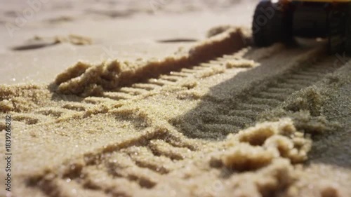 Close-up of tire tracks imprinted in golden beach sand under bright sunlight, creating a textured pattern