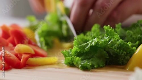 Hands expertly chopping fresh organic lettuce, vibrant red tomatoes, and yellow bell peppers on a rustic wooden board, preparing a delicious and healthy meal promoting wholesome eating habits