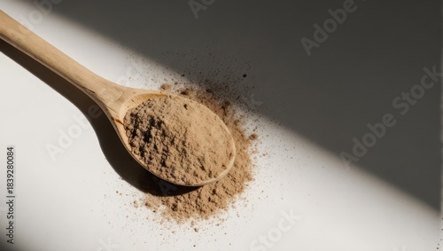 Close-up of a wooden spoon holding brown powder, on a white surface with shadows