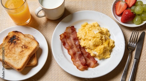 Morning Scrambled egg, bacon breakfast with orange juice, milk, fruit, bread on white plate.
