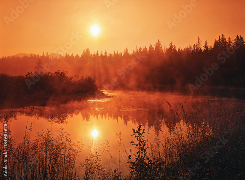 sunrise in the adirondack mountains in a creek near lake placid with reflection of morning fog and brilliant rising sun in orange