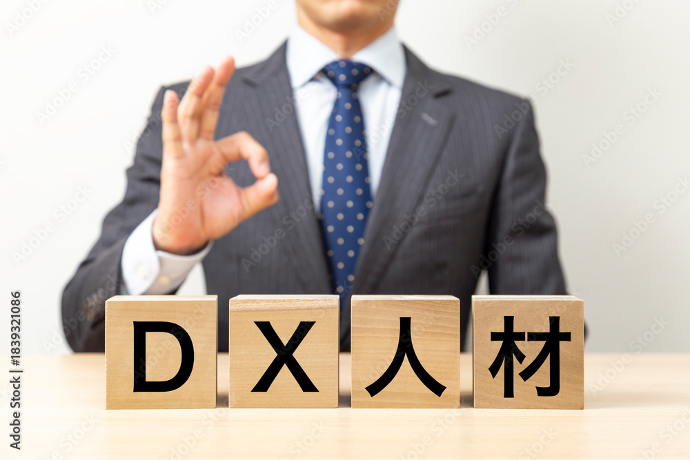 Obraz premium 「DX人材」と書かれたブロックとOKポーズをするビジネスマン