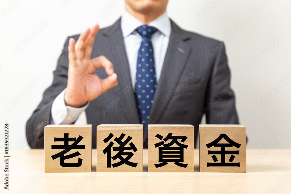 Obraz premium 「老後資金」と書かれたブロックとOKポーズをするビジネスマン