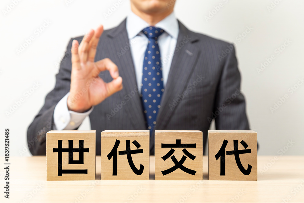 Obraz premium 「世代交代」と書かれたブロックとOKポーズをするビジネスマン