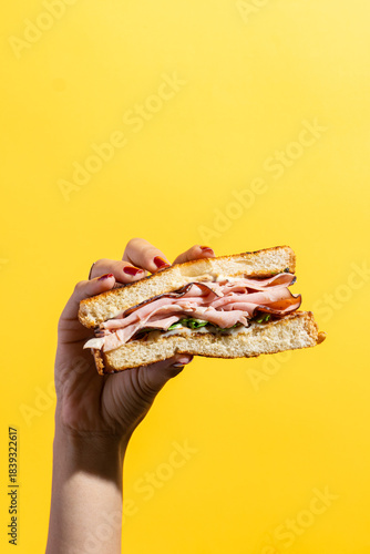 Sándwich de jamón y queso sostenido con la mano sobre fondo amarillo