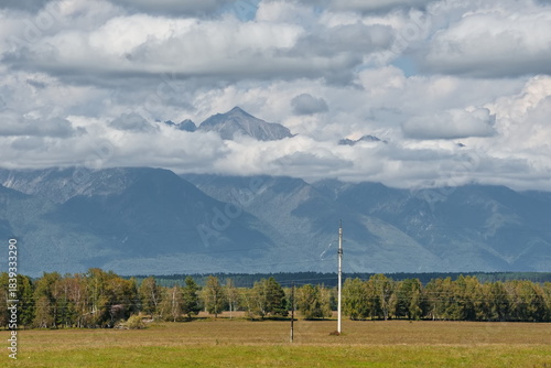 Russia. The Republic of Buryatia. Scenic view of the peaks of the Eastern Sayan mountain range drowning in fog and cumulus clouds from the valley of the Irkut River.