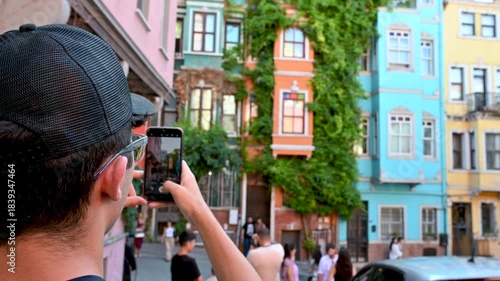 Istanbul, Turkey, August 1, 2025. A young man takes photos with his cell phone of the colorful facades of the historic Balat neighborhood. Iconic in their vibrant colors, the background blurred