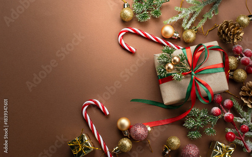 Christmas background with handmade gift box with bow, decorative candy cane, fir branch, ball and cones for tree decoraton. New Year winter holiday ornaments, presents, decor and copy space, top view.