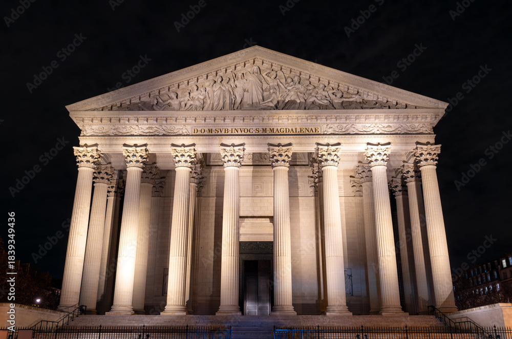 Obraz premium Illuminated La Madeleine church stands with Corinthian columns in Paris, France. Neoclassical Catholic temple features majestic stone facade and pediment sculpture under night sky