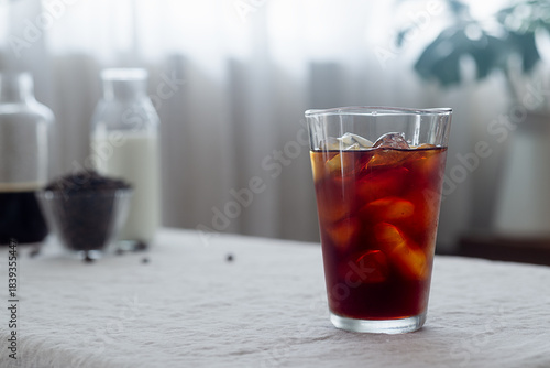 Cold brew coffee in a clear glass with ice on a table covered with a natural linen tablecloth.