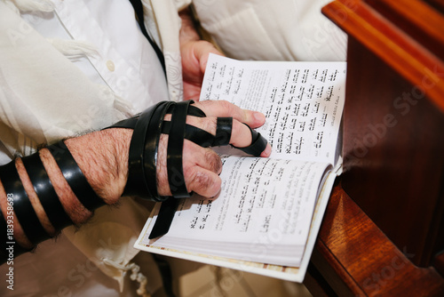 Close-up of Jewish Man's Hand Wearing Tefillin and Reading from a Holy Book or Prayer Book (Siddur) During Religious Study or Bar Mitzvah