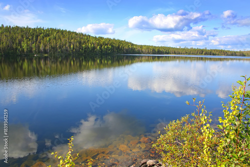 Beautiful landscape with a calm clear lake which has reflections of the trees and clouds. The lake lies within the Arctic circle near Polcirkeln, Northern Sweden, Scandinavia.